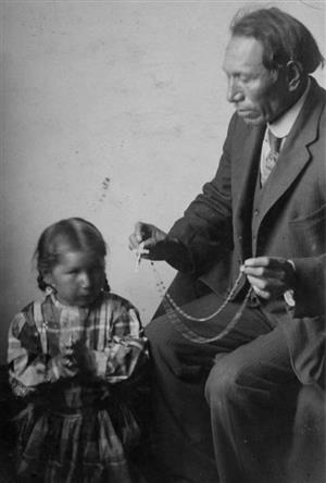 Black Elk holds a rosary with a child standing nearby